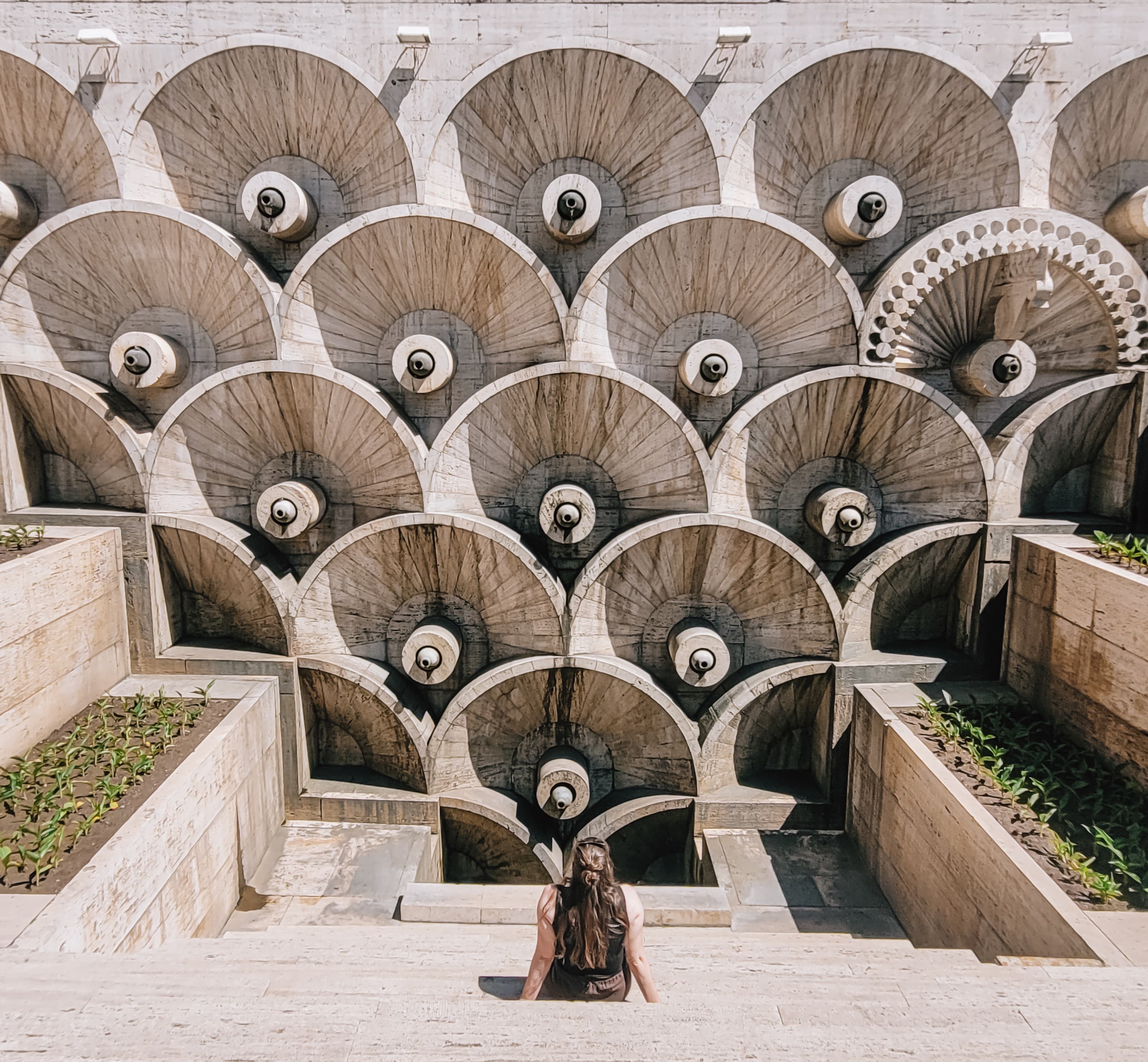 Vrouw zit voor een monumentale waaierarchitectuur in Tbilisi, Georgië